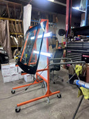 Car windshield on an orange stand in a workshop setting with tools and equipment around.
